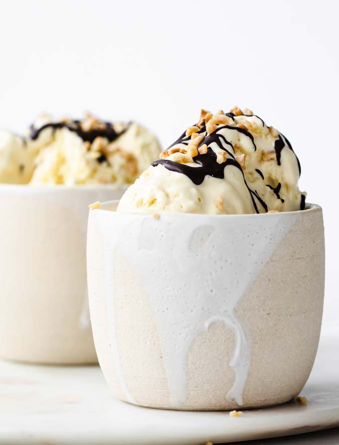 Two white ceramic dessert bowl with homemade low carb vanilla ice cream, decorated with a chocolate drizzle and chopped nuts