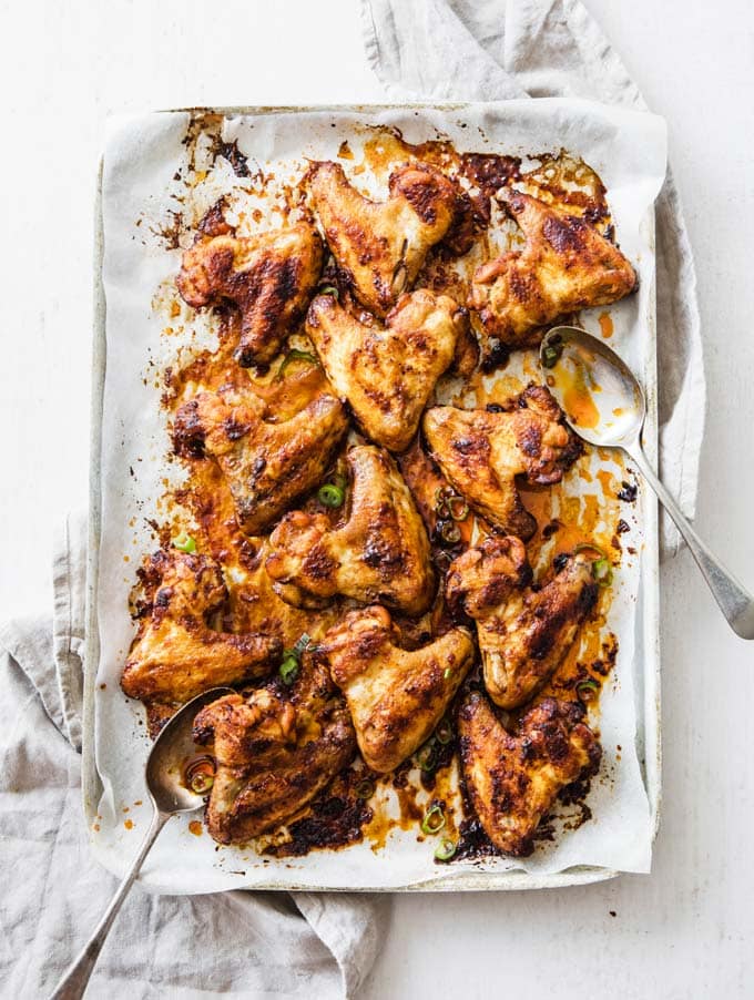 chicken wings on a baking tray lined with parchment paper, and two spoons