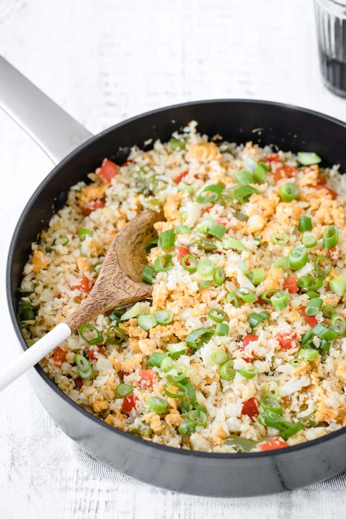 Closeup of cauliflower fried rice with spring onions and pepper in a cast iron pan