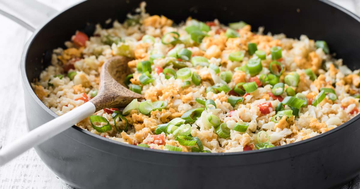 a pan with cauliflower egg fried rice and a wooden spoon