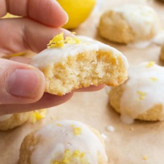 hand holding a bitten glazed lemon cookie with the moist inside visible and more cookies with lemon glaze on parchment paper