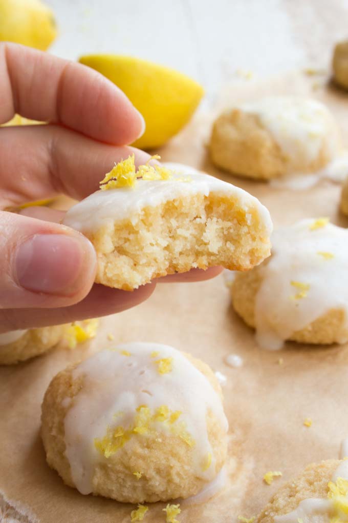 hand holding a bitten glazed lemon cookie with the moist inside visible and more cookies with lemon glaze on parchment paper 