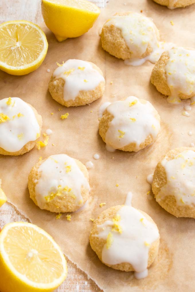 Keto lemon cookies with a lemon glaze and sprinkled with zest on a sheet of baking paper and lemon halves