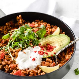 low carb chili with turkey mince in a pan topped with coriander, avocado and sour cream and a spatula