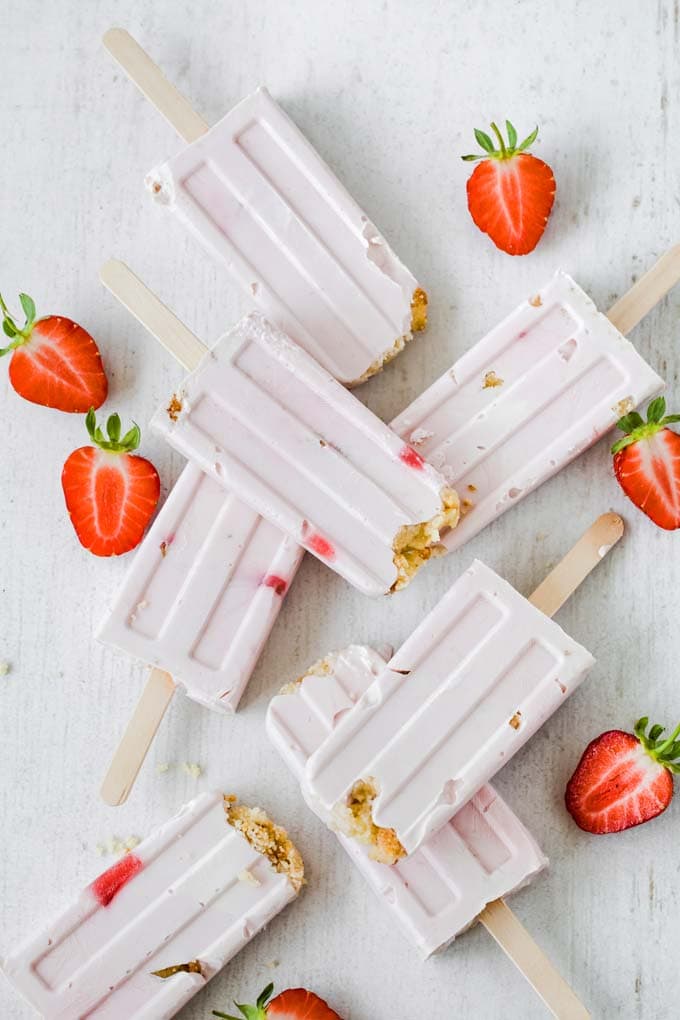 sugar free strawberry cheesecake ice pops on a white surface and strawberries