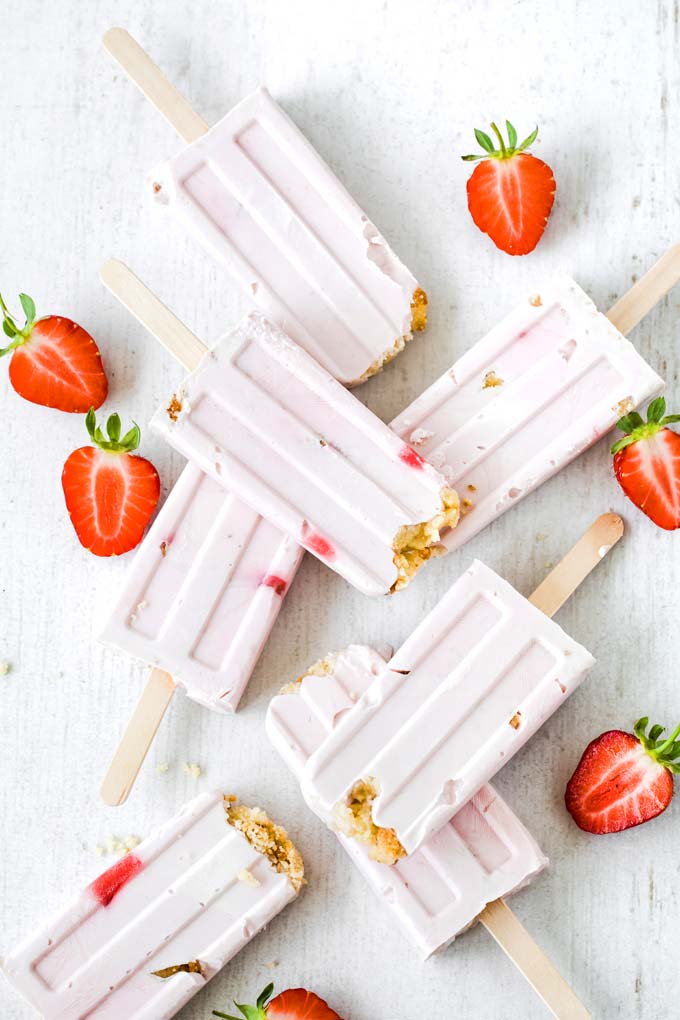 sugar free strawberry cheesecake ice pops on a white surface and strawberries