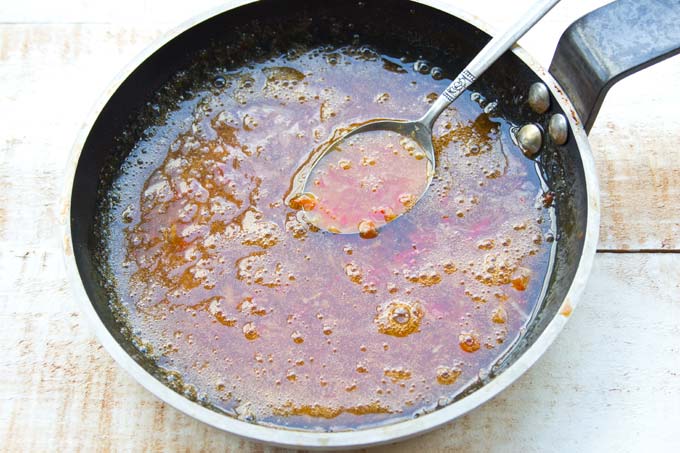 cooking sweet chilli sauce in a frying pan and a spoon stirring