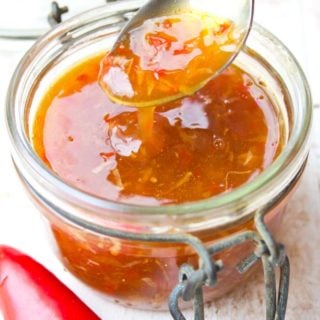 Spoon filled with sweet chilli sauce, which is dripping into a jar of more sauce and a red chilli on the side