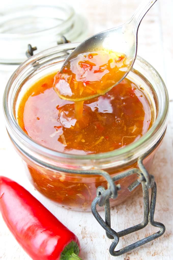 Spoon filled with sweet chilli sauce, which is dripping into a jar of more sauce and a red chilli on the side