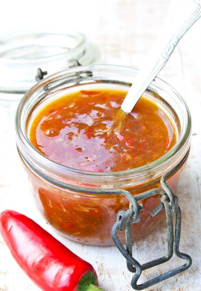 sugar free sweet chilli sauce in a glass jar with a spoon and a chilli on the side