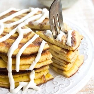 a fork taking a slice of a stack of low carb pancakes with a cinnamon swirl and cream cheese frosting