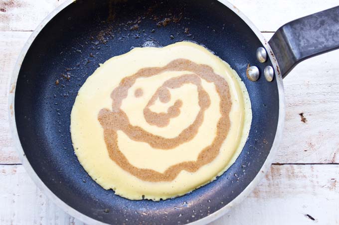 A half cooke pancake with a cinnamon swirl in a frying pan.