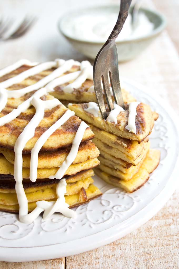 A fork taking a slice of a stack of pancakes with a cinnamon swirl and cream cheese frosting