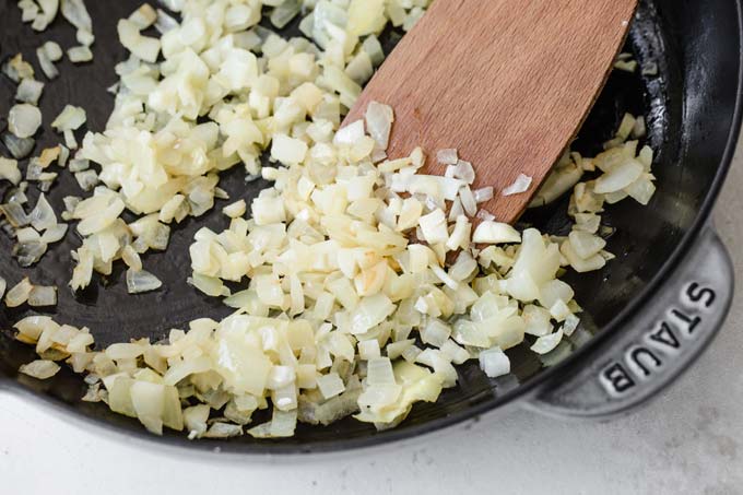 diced white onions frying in a pan and a spatula