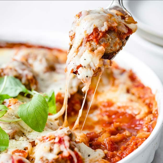 spoon lifting a meatball covered in melted cheese out of a casserole dish