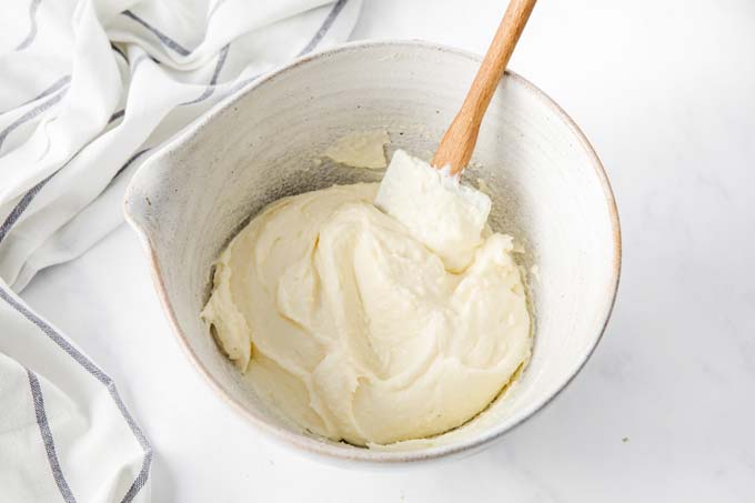 Cream cheese frosting in a white bow with a spatula.