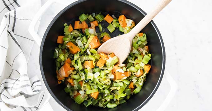 Frying mixed chopped vegetables in a pot with a wooden spoon.