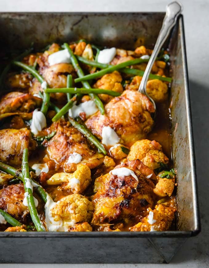 a silver baking tray filled with Keto chicken curry topped with green beans and yoghurt