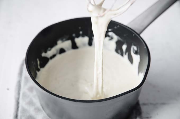 whisking cheese sauce in a pot with a whisk