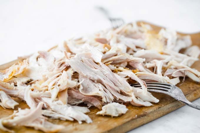 Shredded roast chicken on a wooden board.