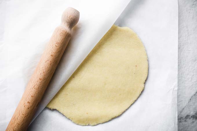 rolled out fathead dough between two sheets of parchment paper and a rolling pin