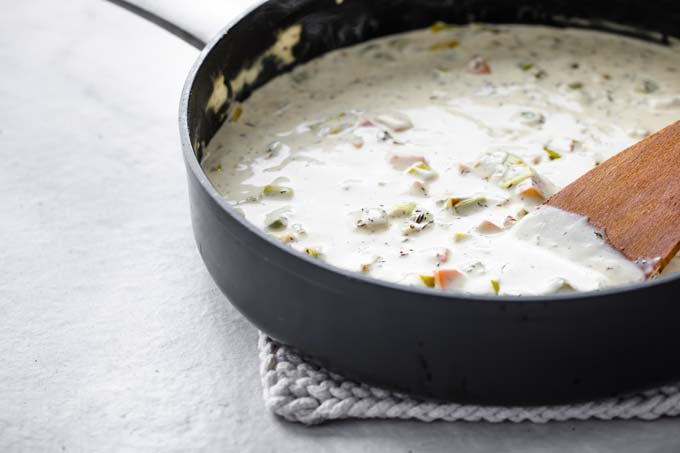 Adding cream to sauteed vegetables in a pan.