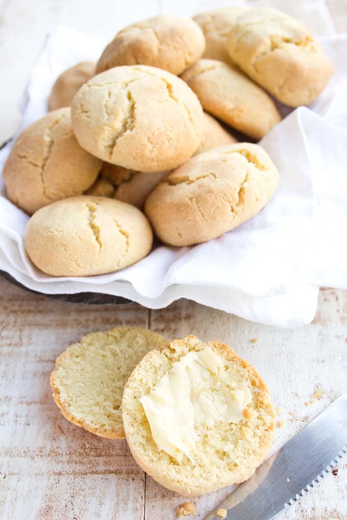 A cut open biscuit spread with butter in front of a bread basket.