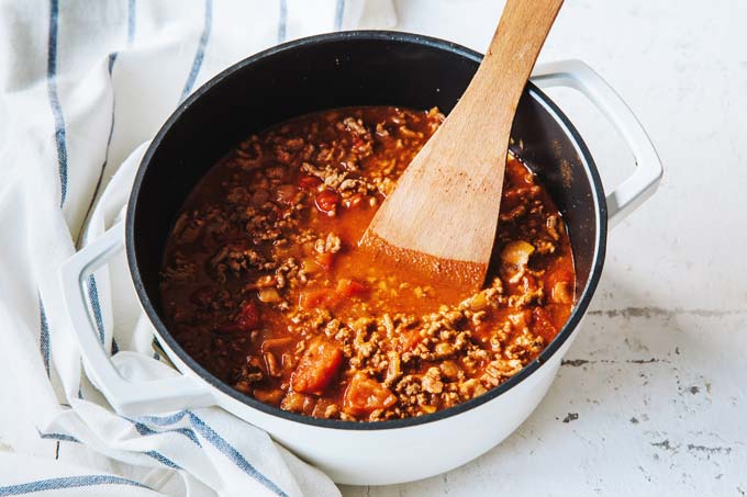 Stirring ground beef and tomato sauce in a saucepan with a spoon.