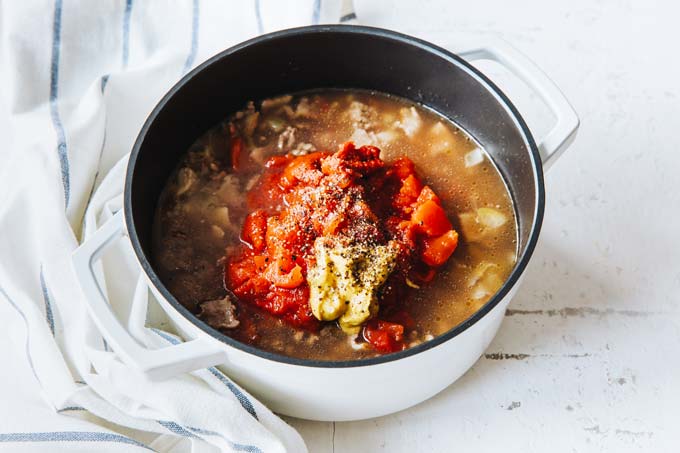 Adding beef broth and tomatoes to ground beef in a saucepan.