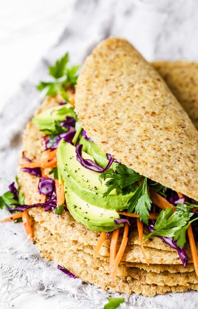 A stack of low carb tortillas with the top tortilla filled with avocado and other vegetables