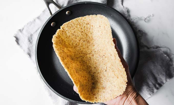 hand holding pliable tortilla over a frying pan