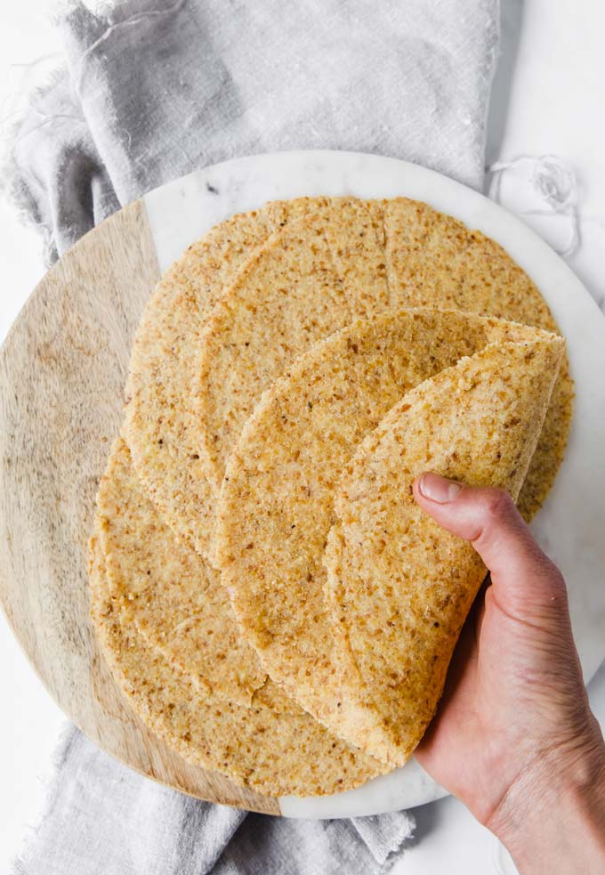 hand showing a pliable low carb tortilla folded in half with more tortillas on a round cutting board
