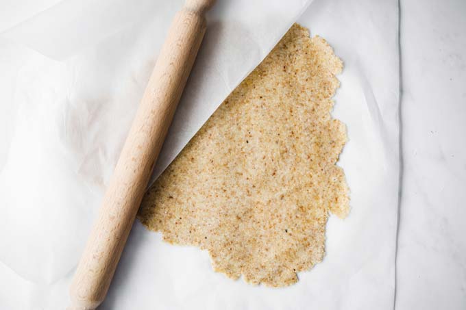 rolling out dough between two sheets of parchment paper with a rolling pin