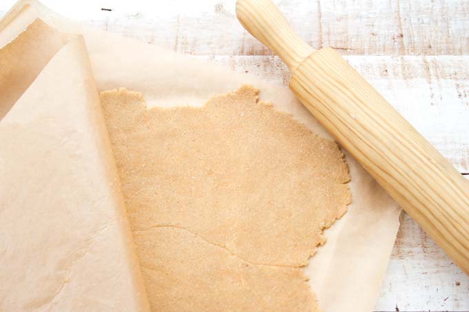 Cookie dough rolled out between two sheets of parchment paper and a rolling pin