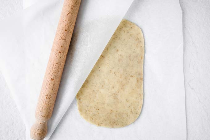 dough rolled out between 2 sheets of parchment and a rolling pin