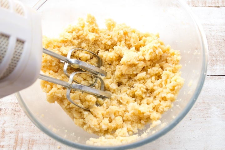 crumbly dough in a glass bowl with electric beaters