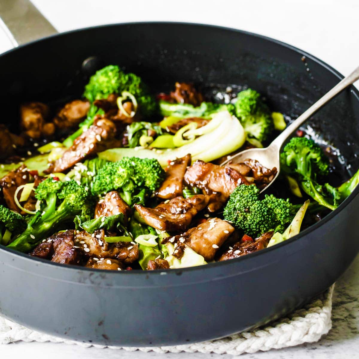 a cast iron pan with keto teriyaki chicken, green vegetables and a spoon