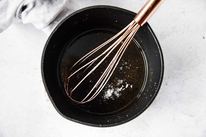 whisking xanthan gum into a sauce in a frying pan with a hand whisk
