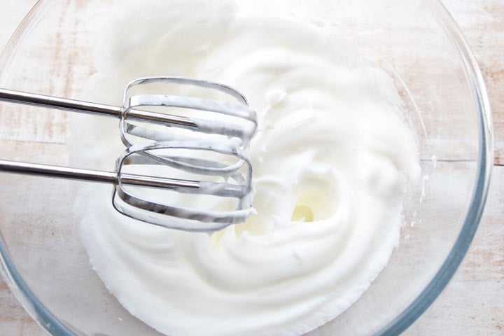 Beaten egg white in a bowl with two whisks.