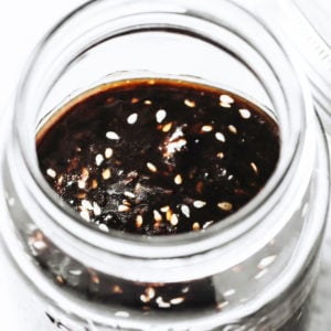 a glass jar filled with sugar free teriyaki sauce topped with sesame seeds