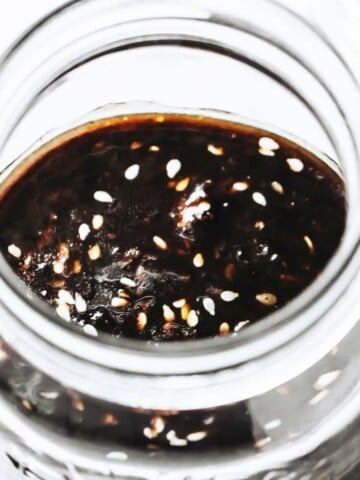 a glass jar filled with sugar free teriyaki sauce topped with sesame seeds