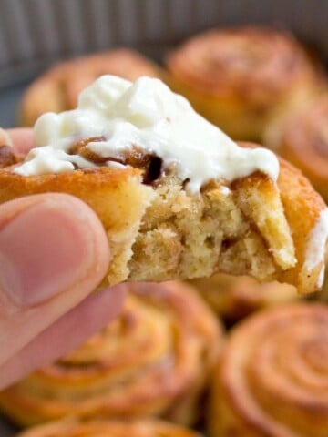 hand holding a keto cinnamon roll topped with cream cheese frosting