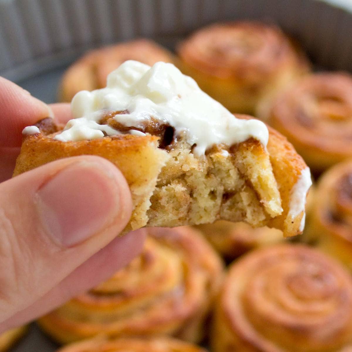 hand holding a keto cinnamon roll topped with cream cheese frosting