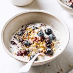 keto overnight oats in a breakfast bowl decorated with coconut, nuts and blueberries and a spoon