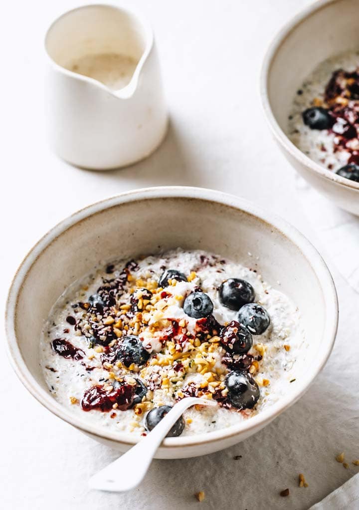 Keto overnight oats with a berry and nut topping in a bowl and a spoon on a set breakfast table