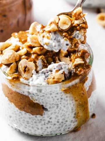 a glass jar with keto chia pudding topped with almond butter and nuts