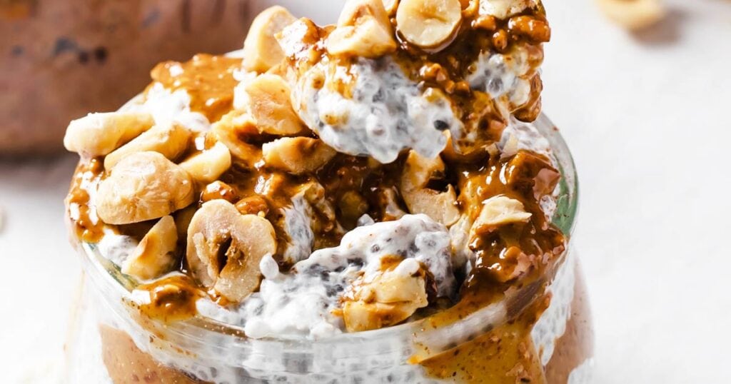 a spoon lifting chia pudding with nuts out of a glass jar