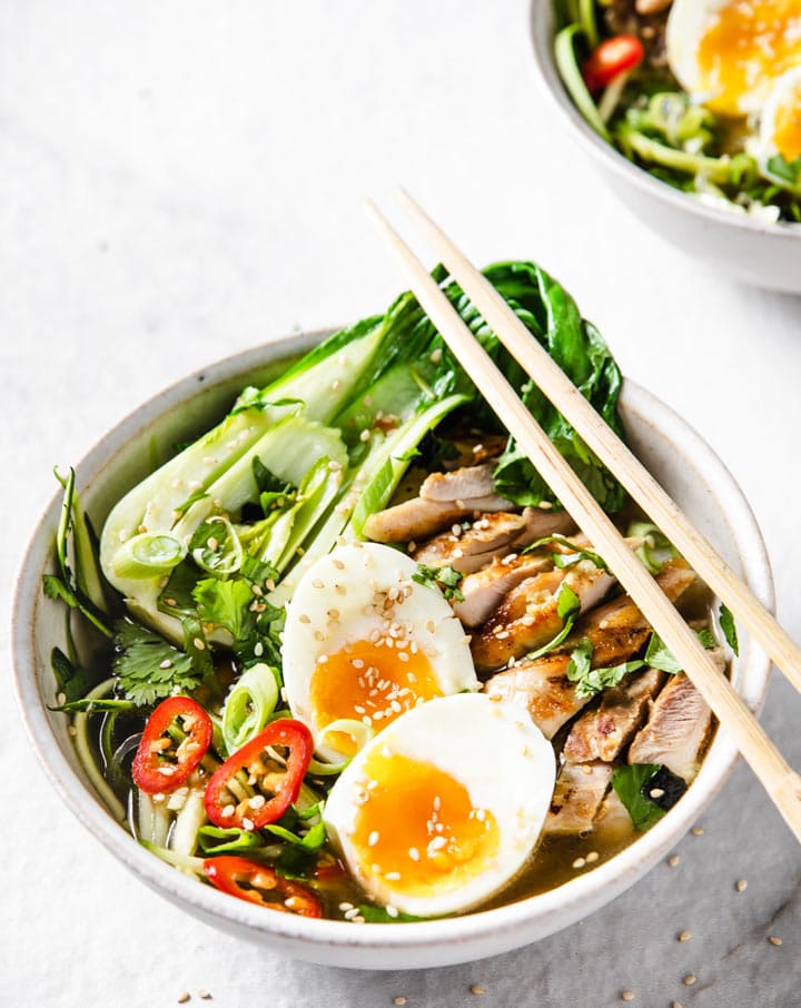 a bowl with keto ramen cntaining chicken, vegetables and a halved soft boiled egg and chopsticks