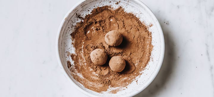 Truffles rolled in a bowl with cacao powder.