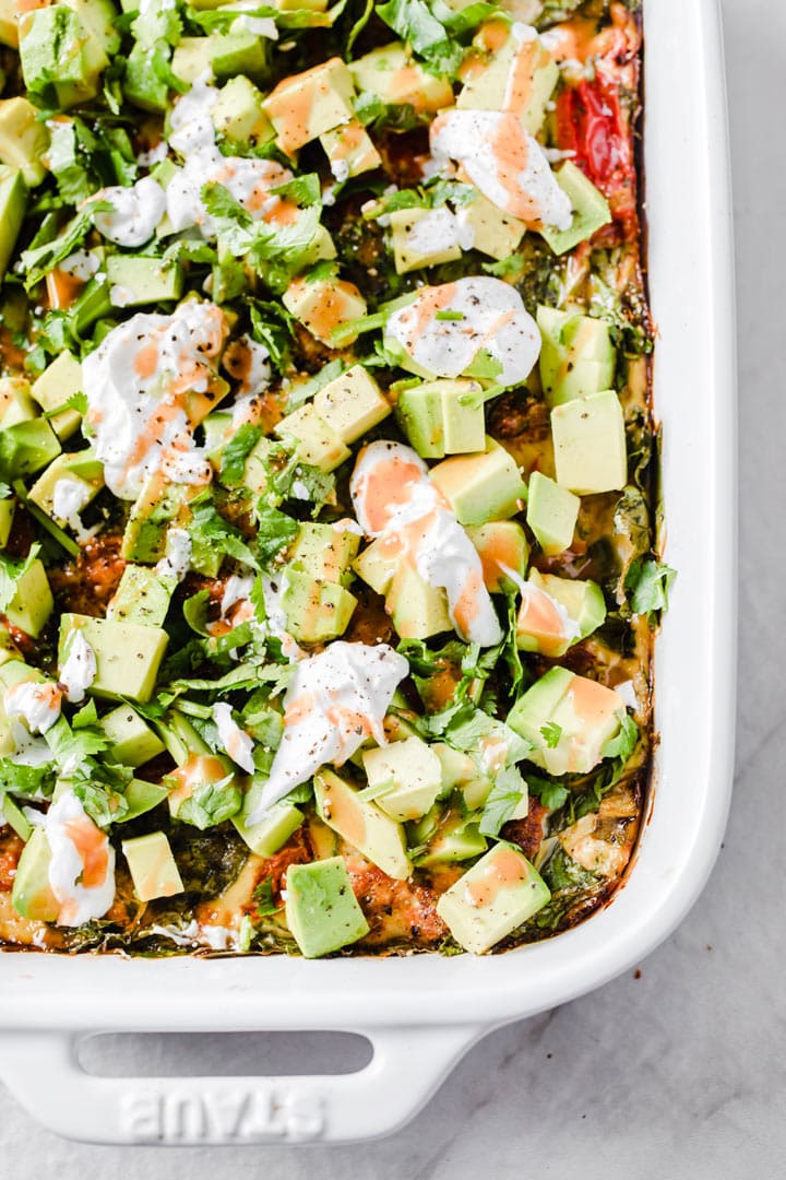 a keto breakfast casserole topped with avocado, coconut yoghurt, coriander and hot sauce
